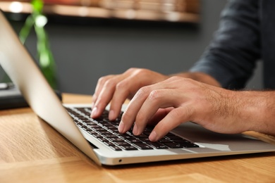 Photo of Man using laptop for search at wooden table indoors, closeup