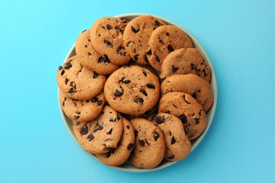 Bowl of delicious chocolate chip cookies on light blue background, top view