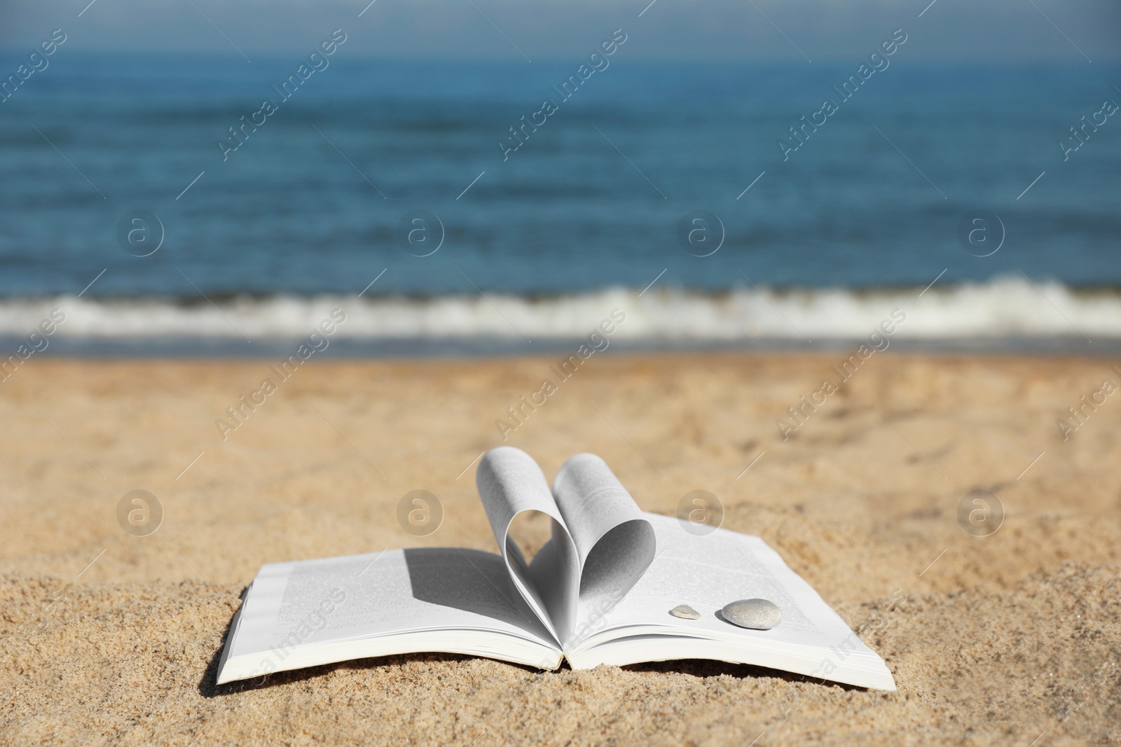 Photo of Open book with pages folded in heart shape on sandy beach near sea