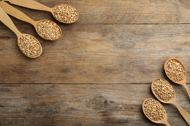 Photo of Uncooked green buckwheat grains in spoons on wooden table, flat lay. Space for text