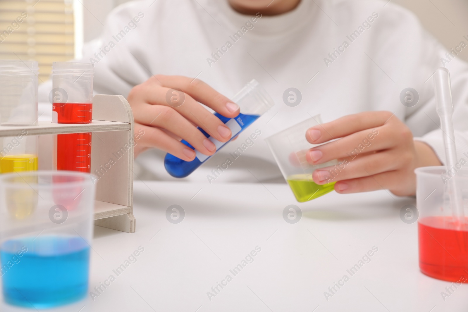 Photo of Girl mixing colorful liquids at white table indoors, closeup. Chemical experiment set for kids