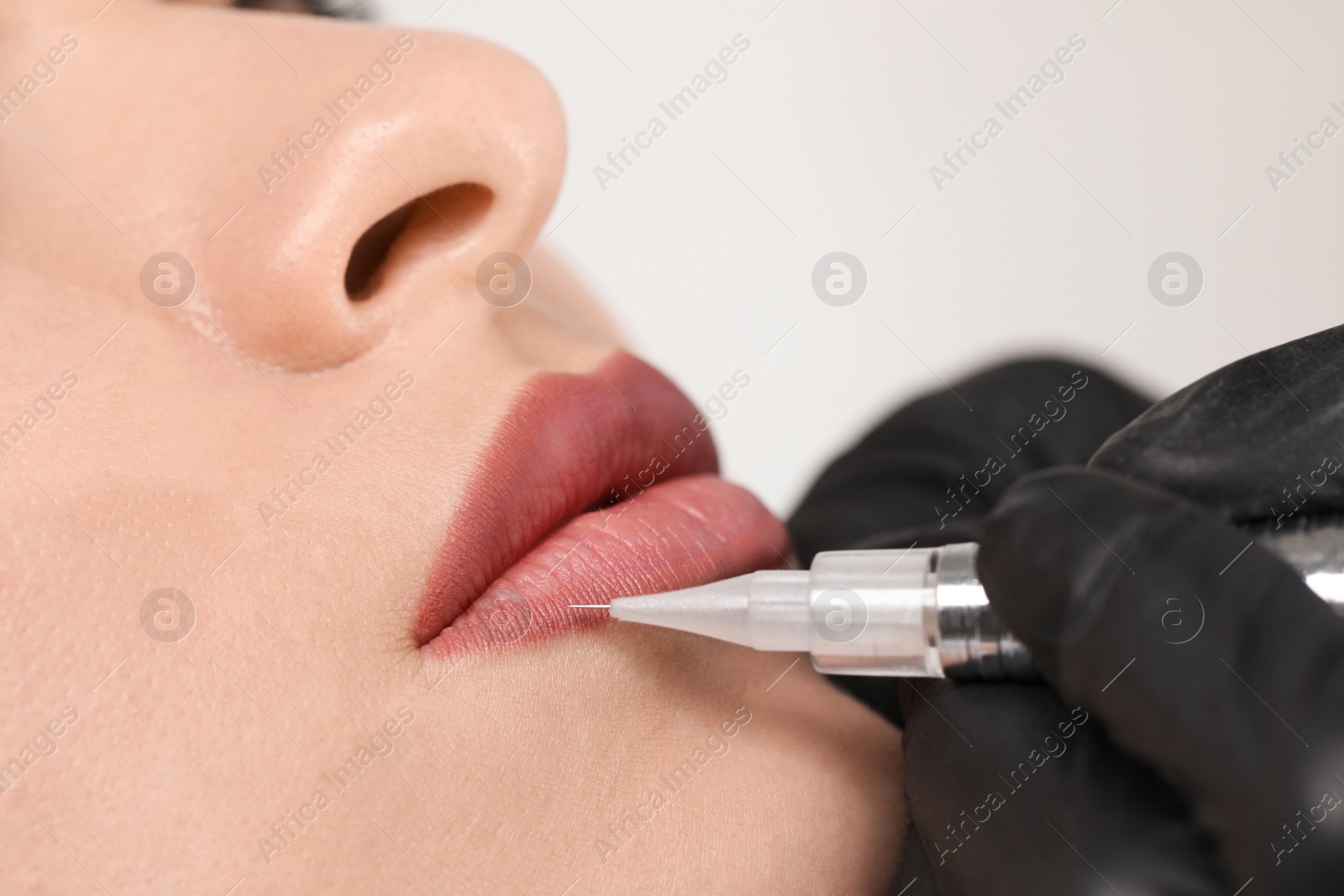 Photo of Young woman during procedure of permanent lip makeup in beauty salon, closeup