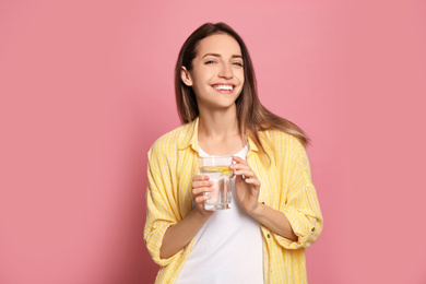 Photo of Young woman with glass of lemon water on pink background