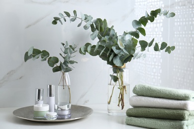 Photo of Fresh eucalyptus branches and cosmetic products on countertop in bathroom