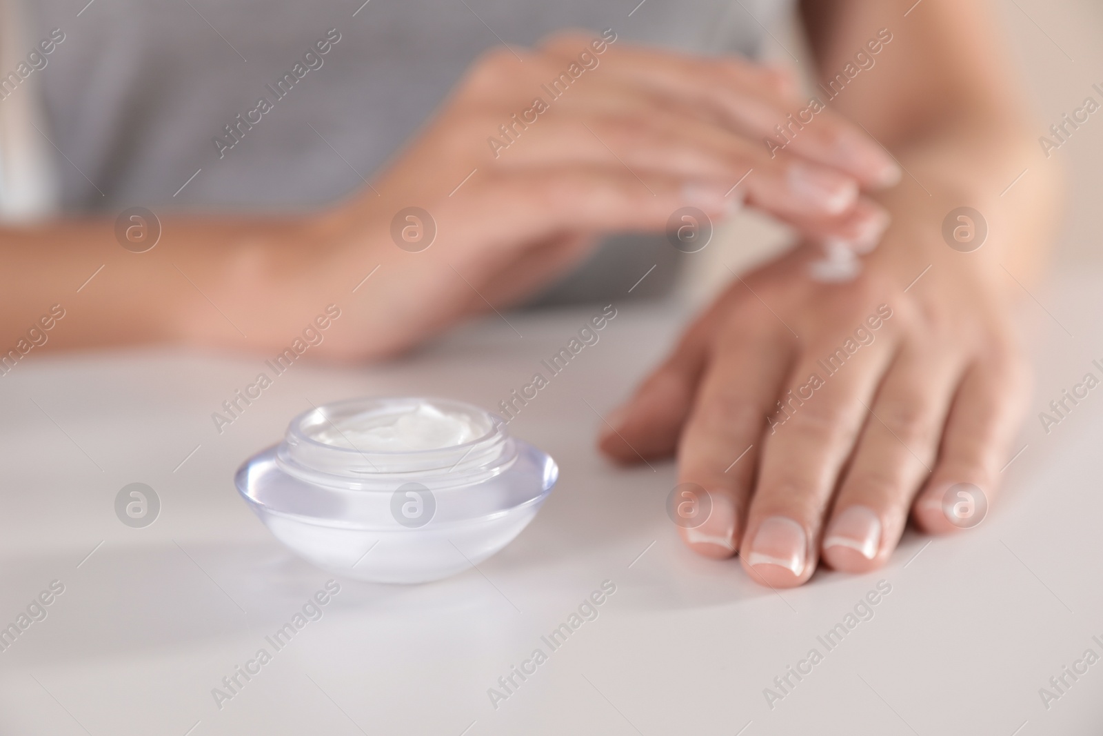 Photo of Young woman applying hand cream at table, closeup