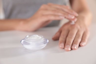 Photo of Young woman applying hand cream at table, closeup
