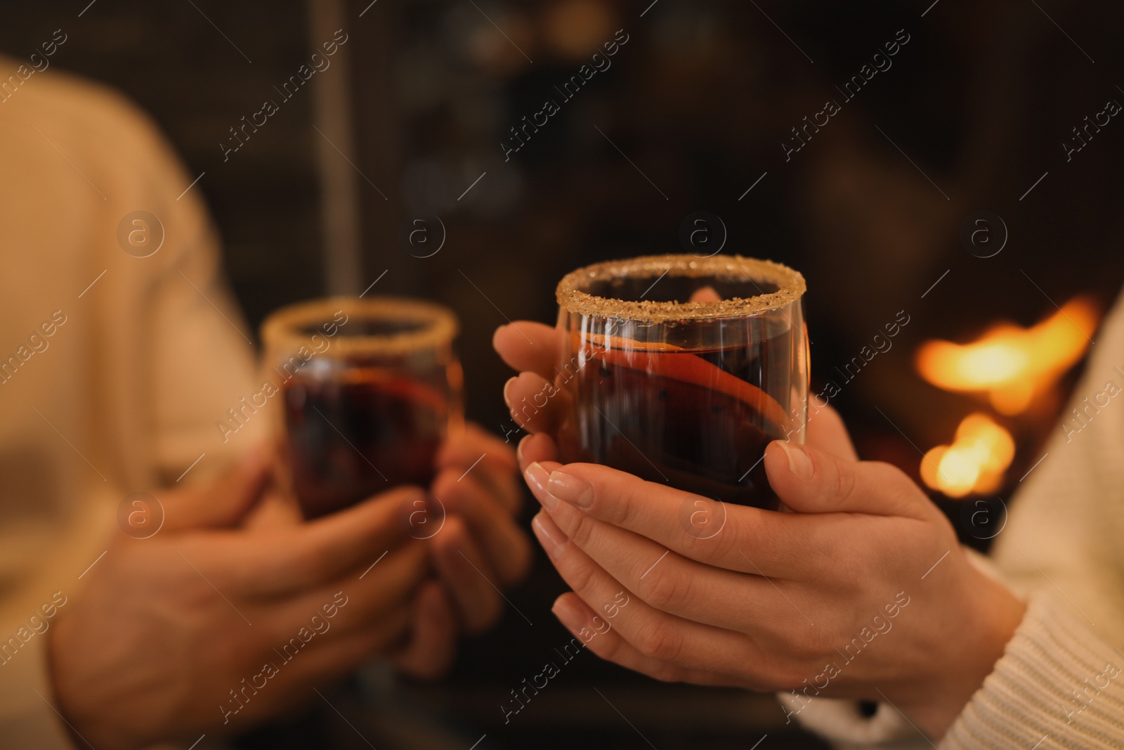 Photo of Couple with tasty mulled wine near fireplace indoors, closeup