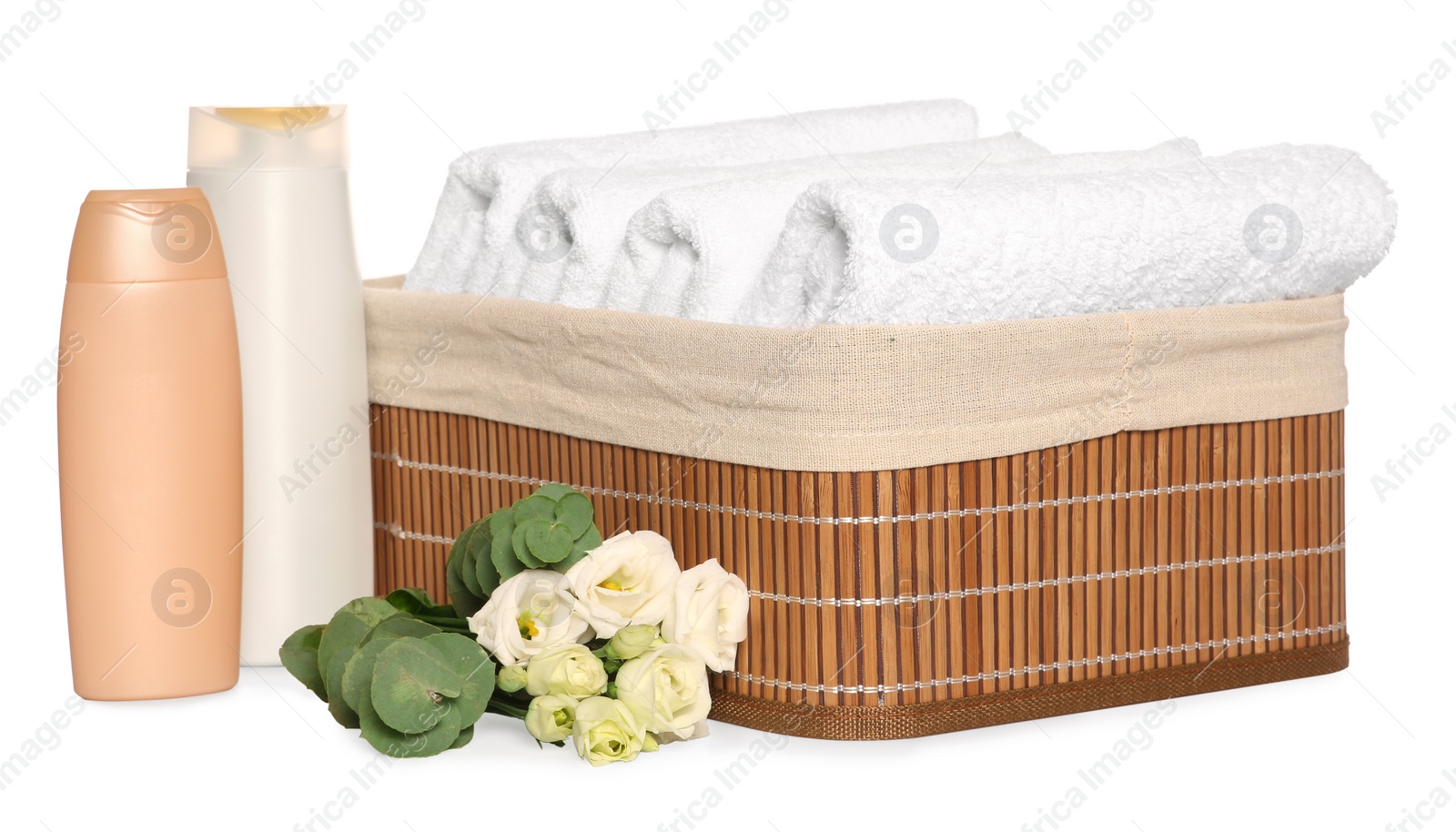 Photo of Wicker basket with folded soft terry towels, cosmetic products and flowers on white background