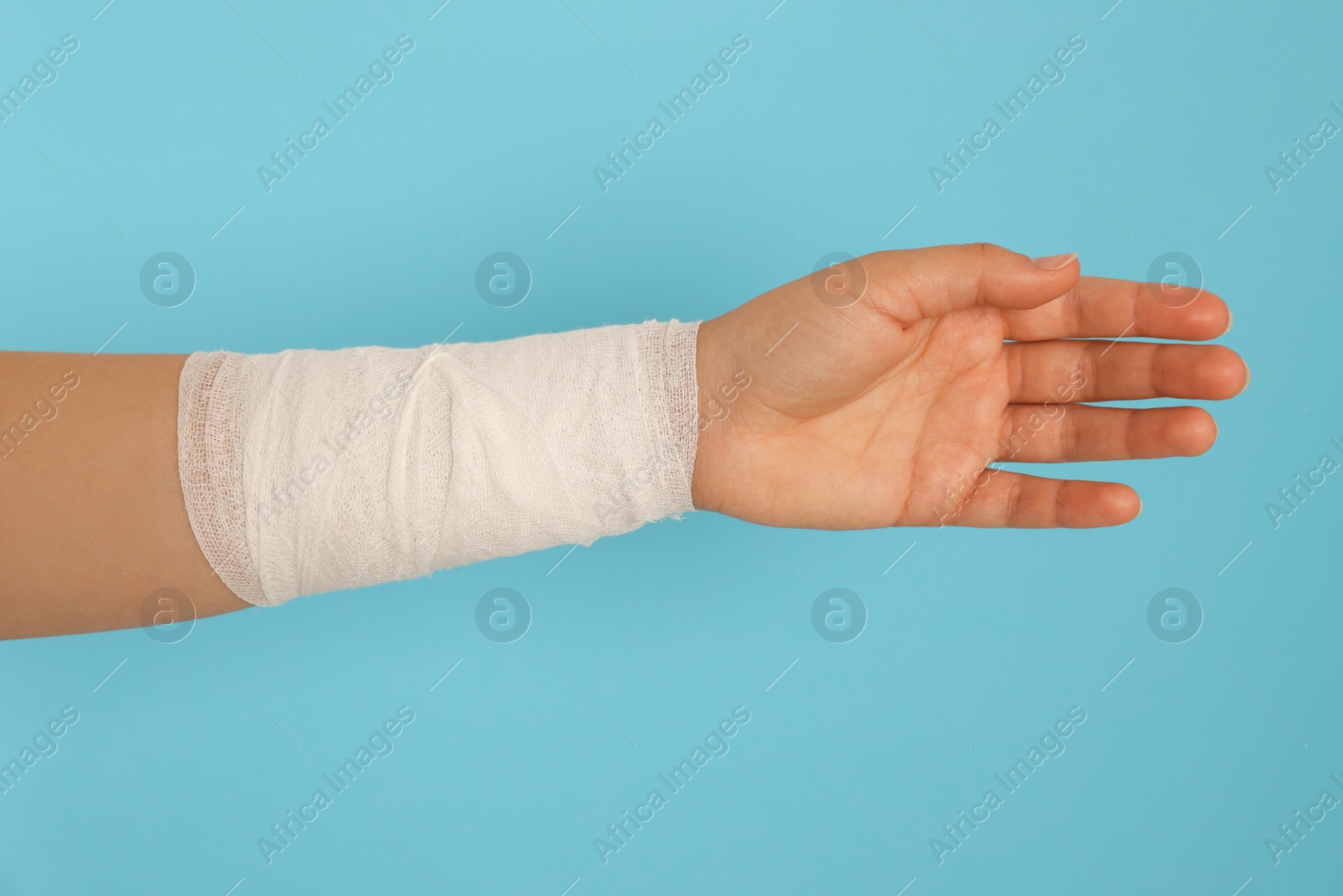 Photo of Woman with wrist wrapped in medical bandage on light blue background, closeup