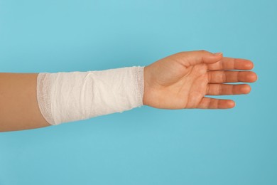 Photo of Woman with wrist wrapped in medical bandage on light blue background, closeup