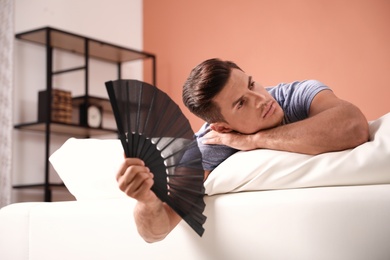 Photo of Man with hand fan on sofa. Summer season