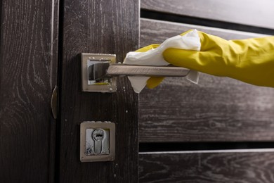 Photo of Woman cleaning door handle with detergent and paper towel, closeup