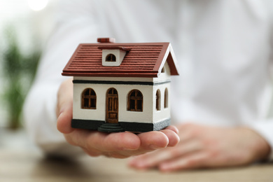 Photo of Real estate agent holding house model indoors, closeup
