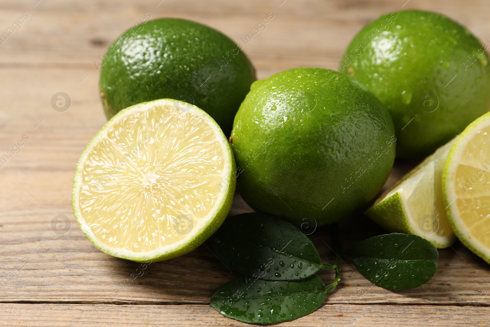 Photo of Fresh ripe limes and green leaves with water drops on wooden table, closeup