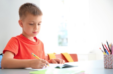 Photo of Cute little child doing assignment at desk in classroom. Elementary school