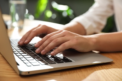 Photo of Young woman using laptop for search at wooden table in room, closeup