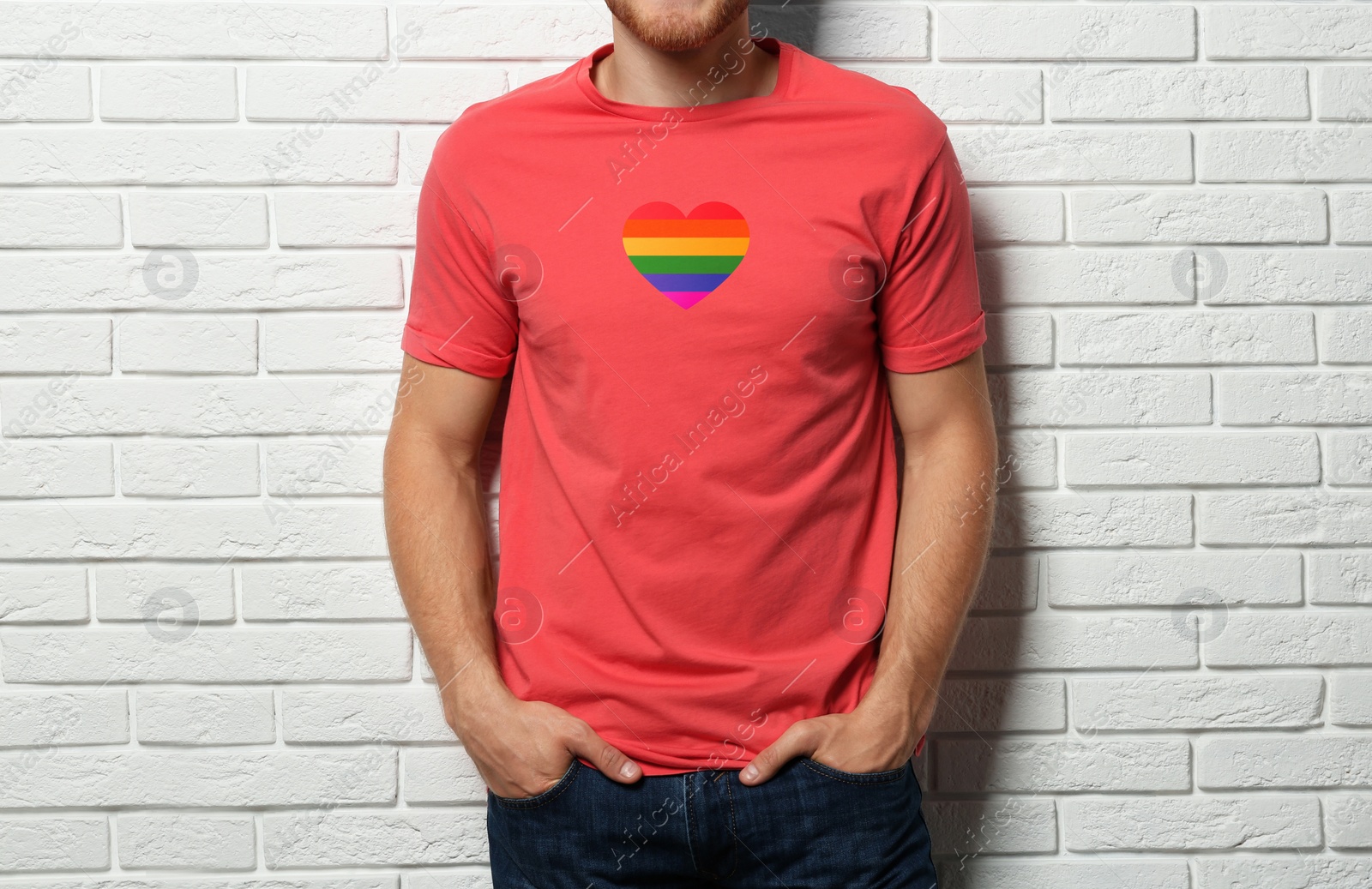 Image of Young man wearing t-shirt with image of heart shaped LGBT pride flag near white brick wall