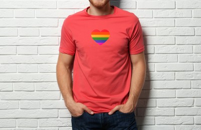 Image of Young man wearing t-shirt with image of heart shaped LGBT pride flag near white brick wall