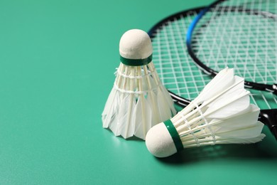 Photo of Feather badminton shuttlecocks and rackets on green background, closeup. Space for text