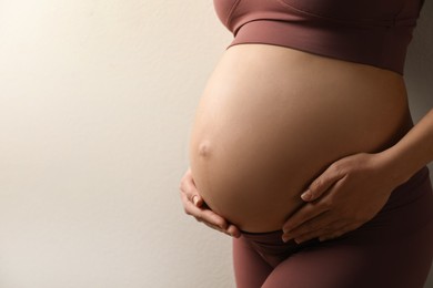 Photo of Pregnant young woman touching belly on beige background, closeup. Space for text