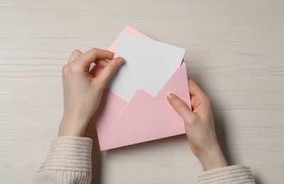 Photo of Woman taking card out of letter envelope at light wooden table, top view