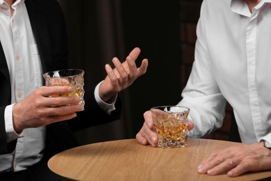 Photo of Men with glasses of whiskey at wooden table indoors, closeup