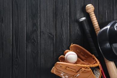 Photo of Baseball glove, bats, ball and batting helmet on black wooden table, flat lay. Space for text