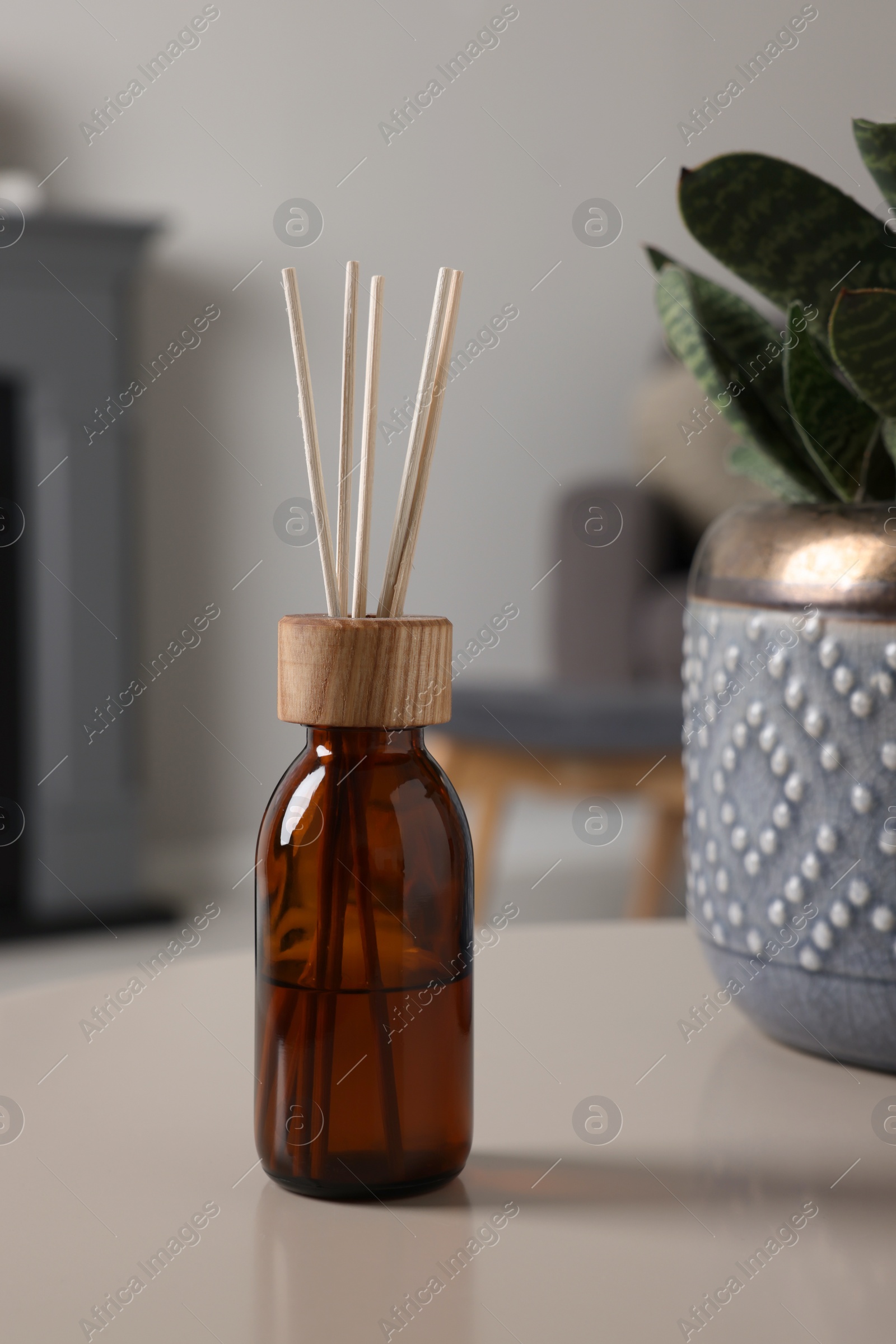 Photo of Aromatic reed air freshener near houseplant on light table indoors