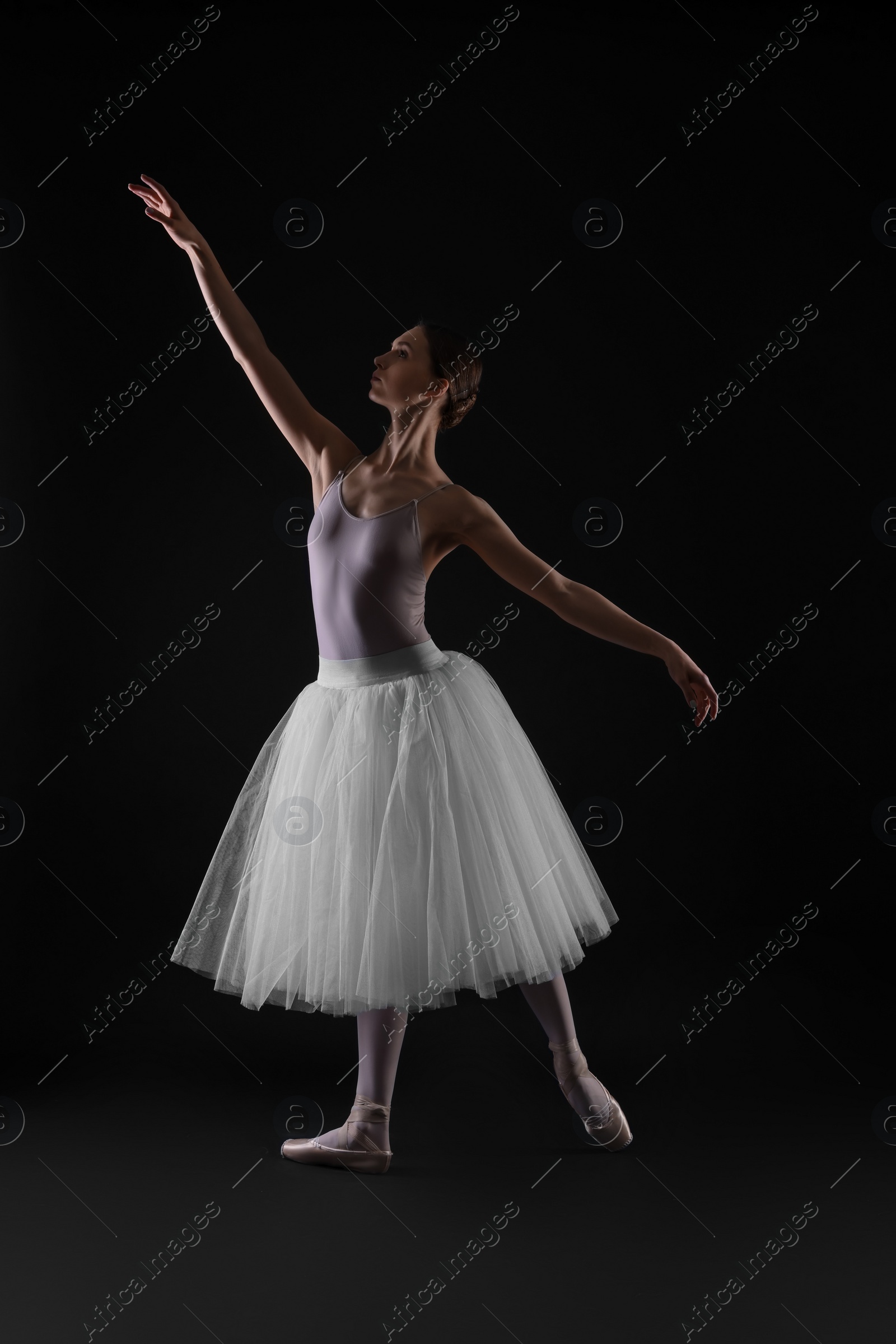 Photo of Young ballerina practicing dance moves on black background