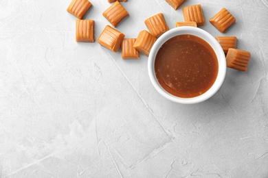 Delicious caramel candies and sauce on light background