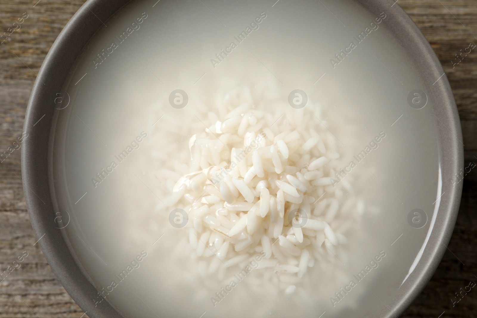 Photo of Bowl with rice soaked in water on wooden table, top view