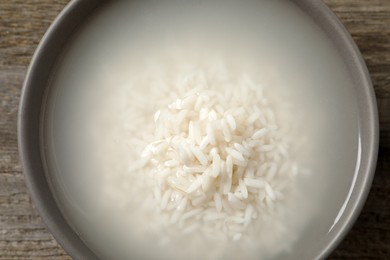 Bowl with rice soaked in water on wooden table, top view