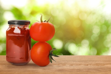 Jar of tomato sauce on wooden table against blurred background, space for text