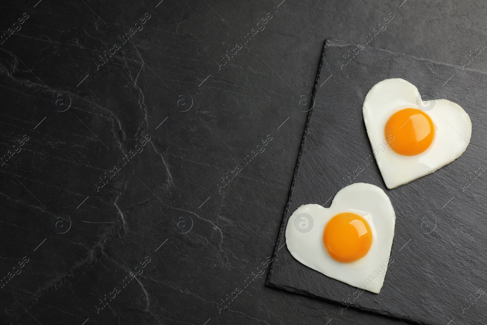 Photo of Heart shaped fried eggs on black table, top view. Space for text