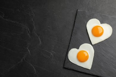 Photo of Heart shaped fried eggs on black table, top view. Space for text