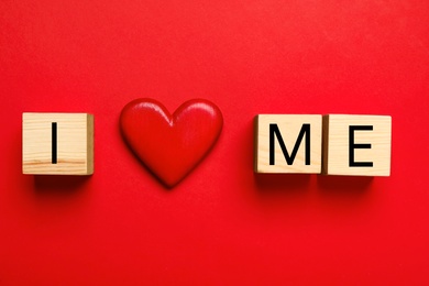 Photo of Phrase I Love Me made with wooden cubes and heart on red background, flat lay