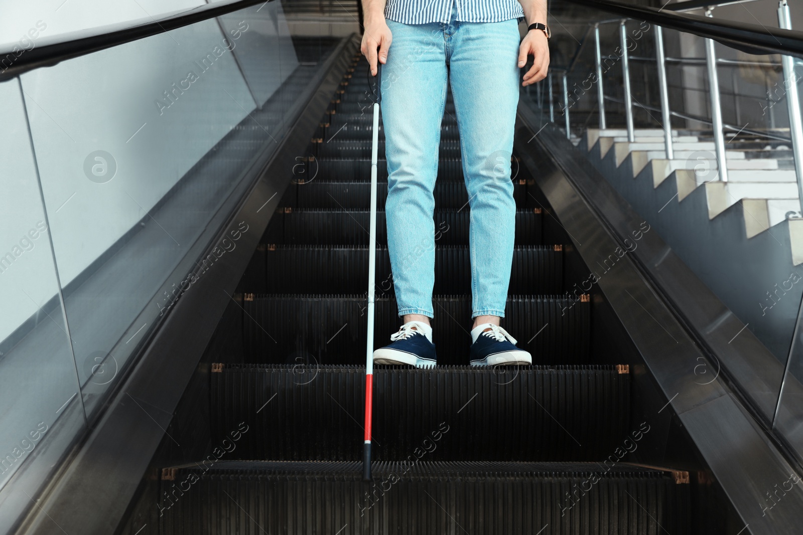 Photo of Blind person with long cane on escalator indoors