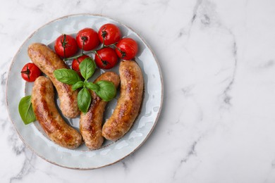 Plate with tasty homemade sausages, basil leaves and tomatoes on white marble table, top view. Space for text