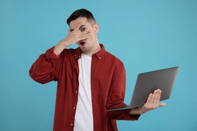 Embarrassed man with laptop covering face on light blue background