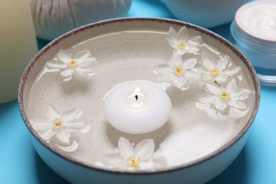 Photo of Spa composition with burning candle and beautiful flowers on light blue background, closeup