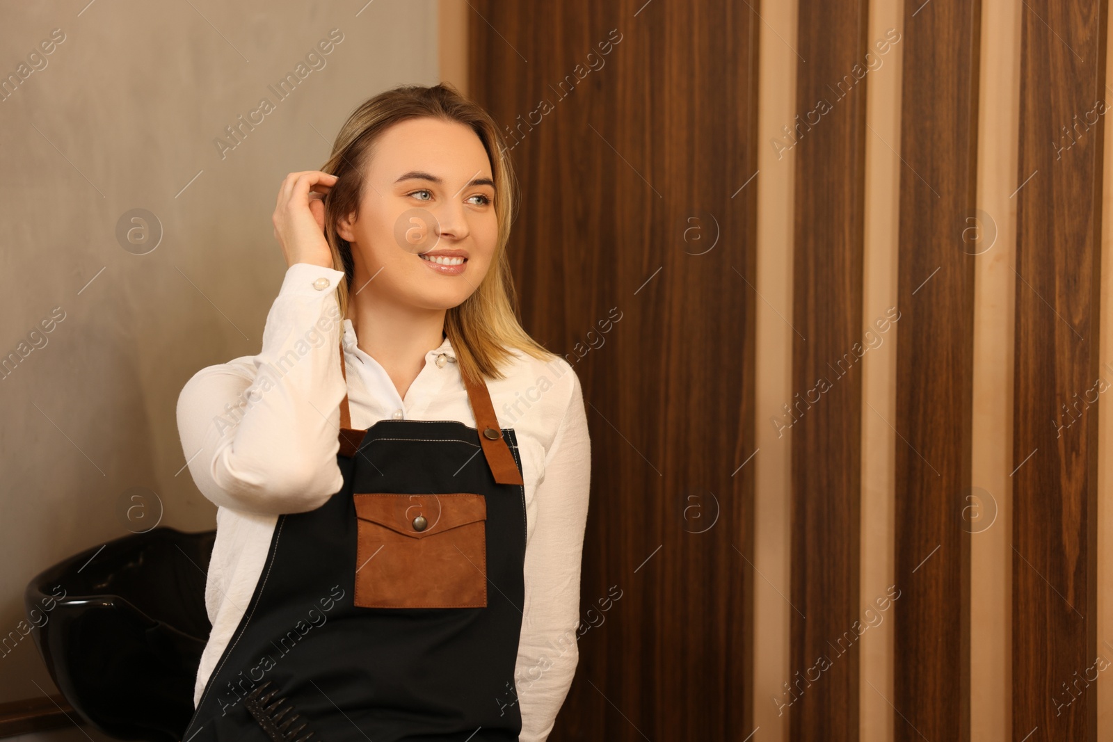 Photo of Professional hairdresser wearing apron in beauty salon, space for text