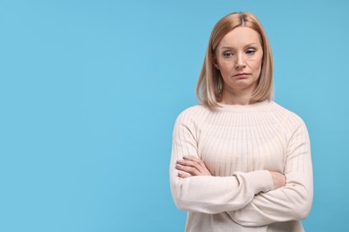Photo of Sad woman with crossed arms on light blue background. Space for text