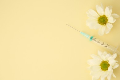 Photo of Medical syringe and chrysanthemum flowers on pale yellow background, flat lay. Space for text