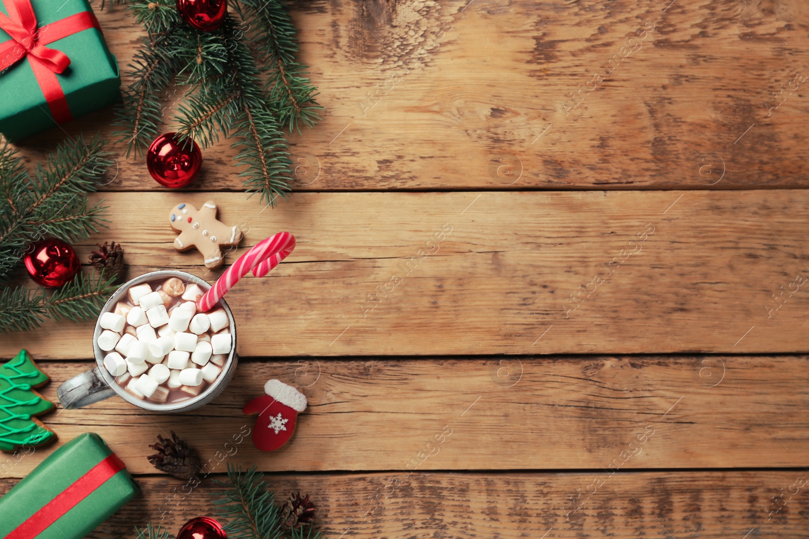 Photo of Delicious hot chocolate with marshmallows and candy cane near Christmas decor on wooden table, flat lay. Space for text