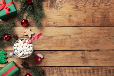 Delicious hot chocolate with marshmallows and candy cane near Christmas decor on wooden table, flat lay. Space for text