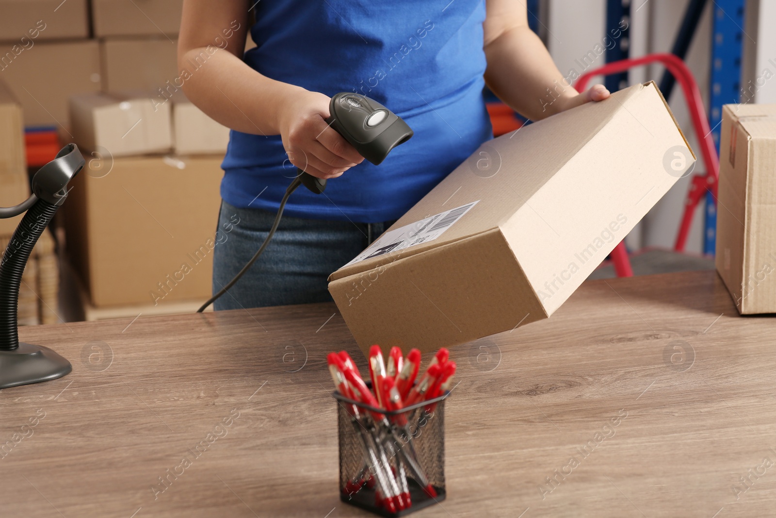 Photo of Post office worker with scanner reading parcel barcode at counter, closeup