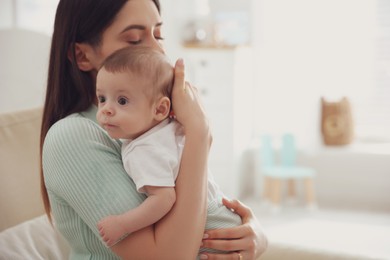 Young woman with her cute baby at home, space for text