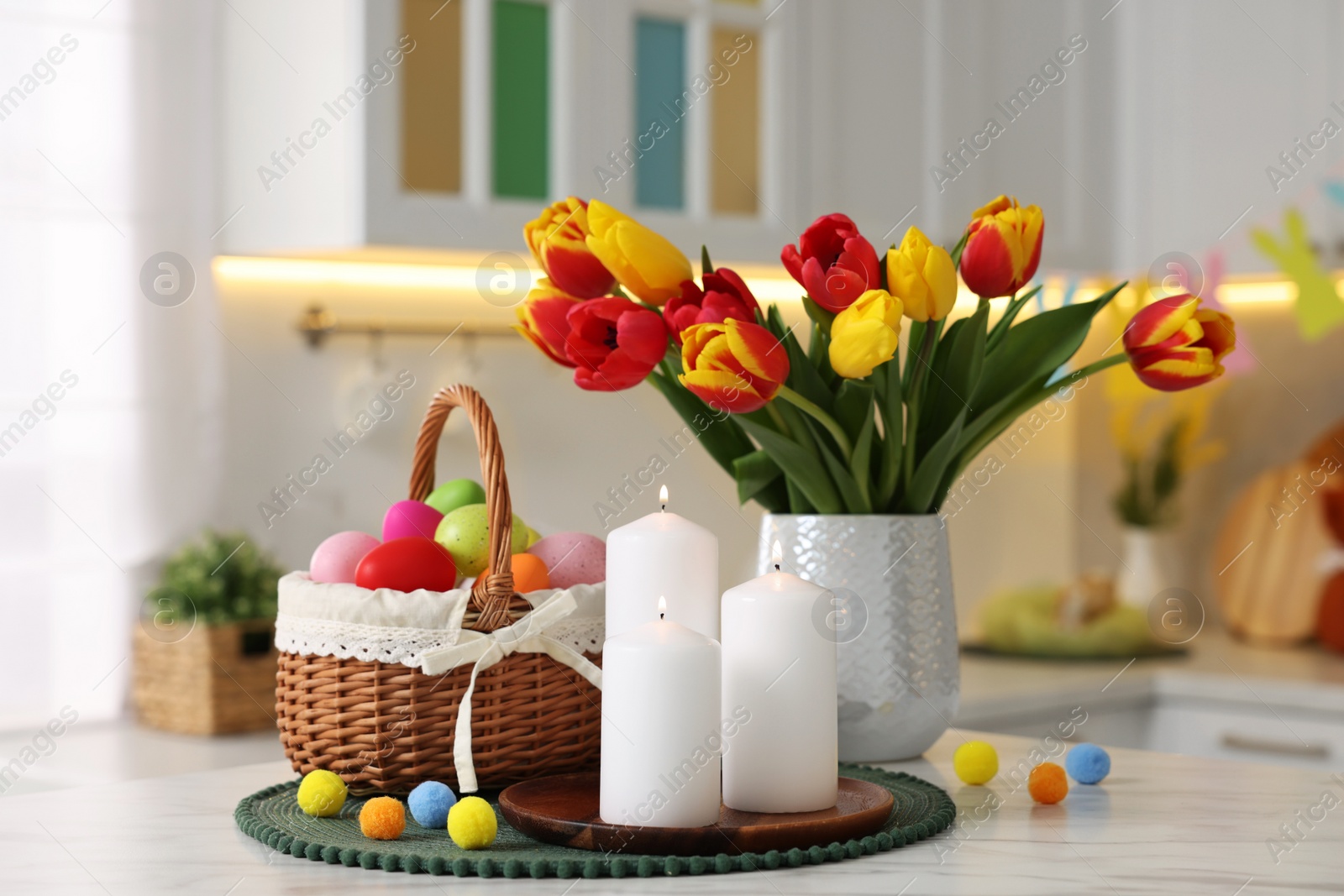 Photo of Easter decorations. Bouquet of tulips, painted eggs and burning candles on table indoors, closeup