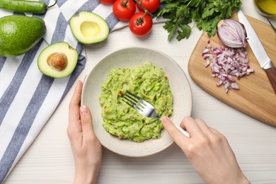 Woman preparing delicious guacamole at white wooden table, top view
