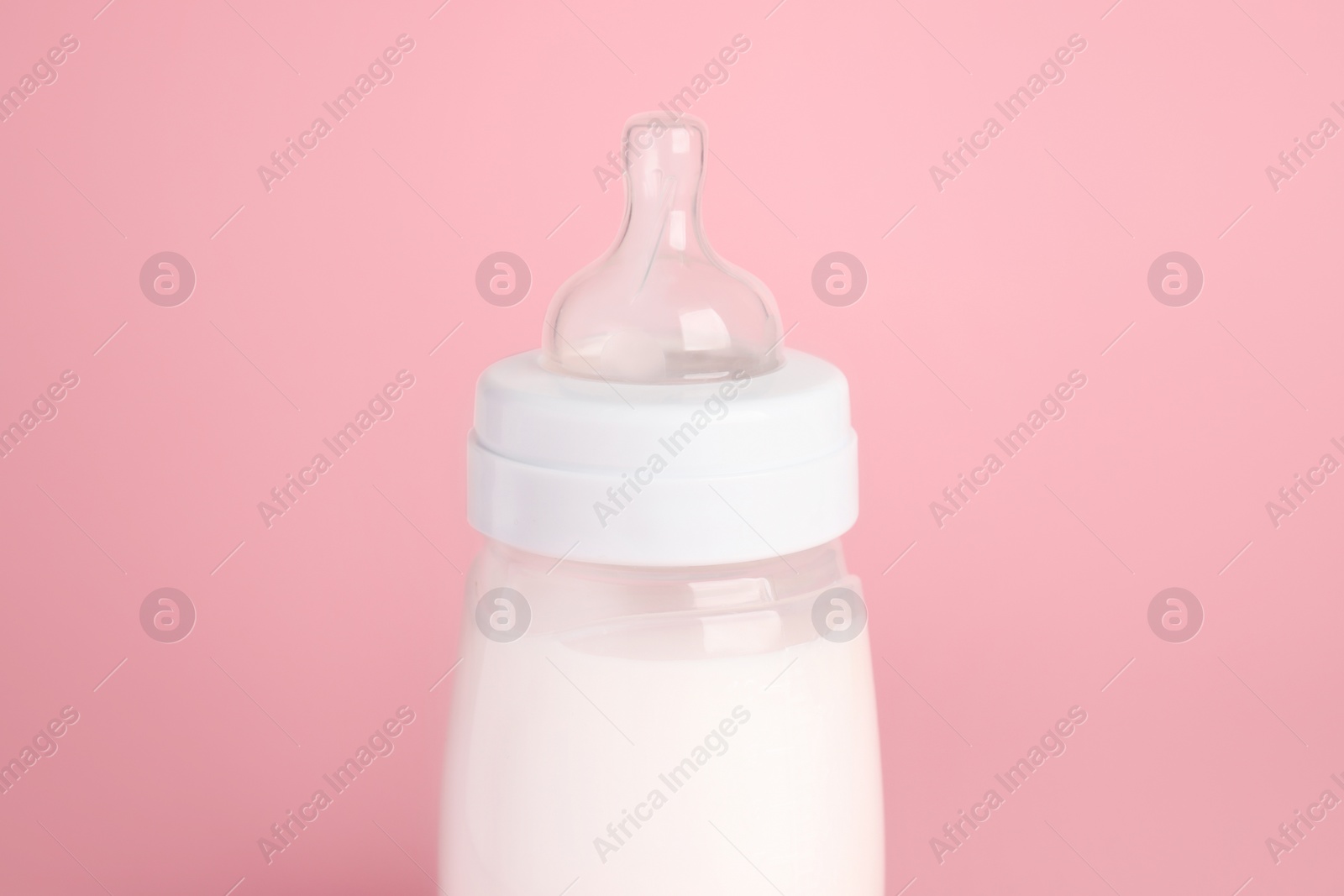 Photo of One feeding bottle with milk on pink background, closeup